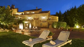 Ein Steinhaus mit einer Terrasse, die zwei Lounge-Stühle, einen Tisch und Kübelpflanzen umfasst.