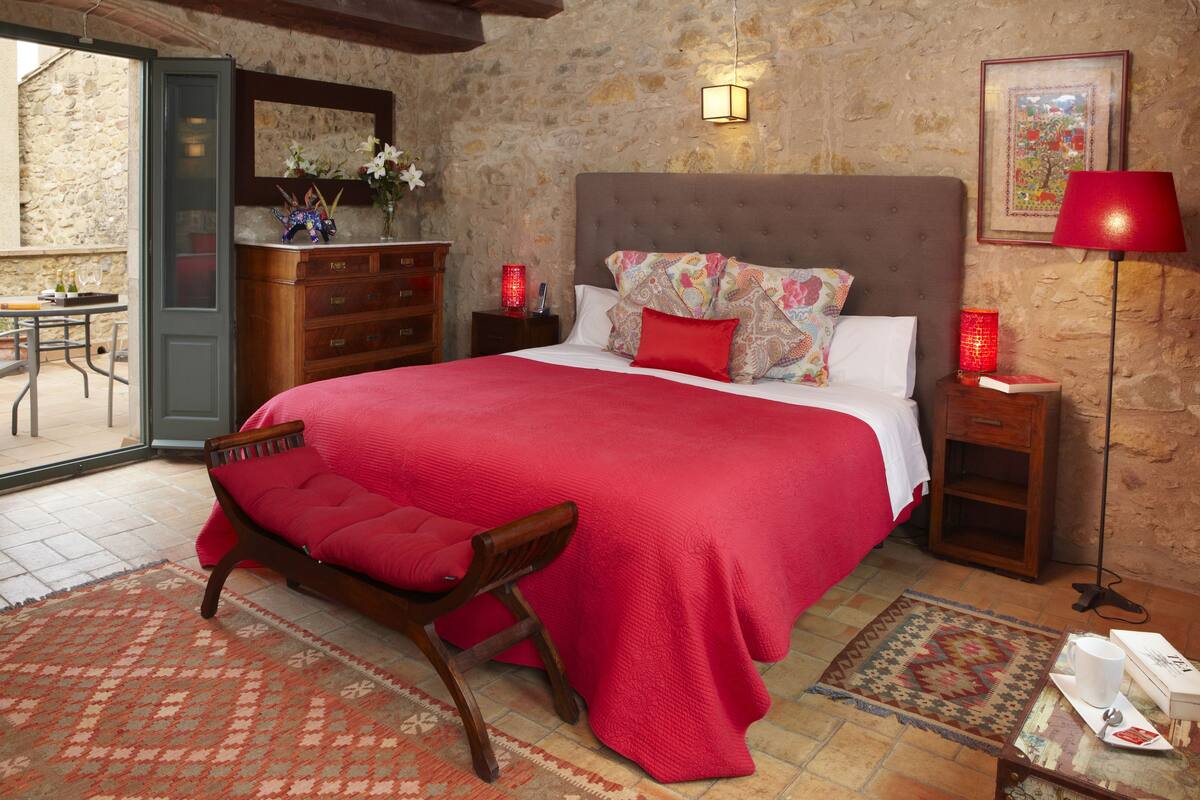 Een slaapkamer met een groot bed, een houten stoel, een dressoir, een nachtkastje, een lamp en uitzicht op buiten.