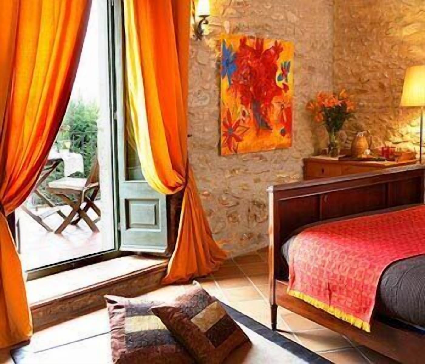 Ein Schlafzimmer mit einem Bett, einer Steinwand, einem Fenster mit Vorhängen und einem Gemälde an der Wand.