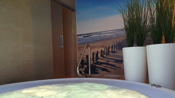 A hot tub with a view of a beach and a wooden pier. - Hotel Friesische Wehde (Bockhorn)
