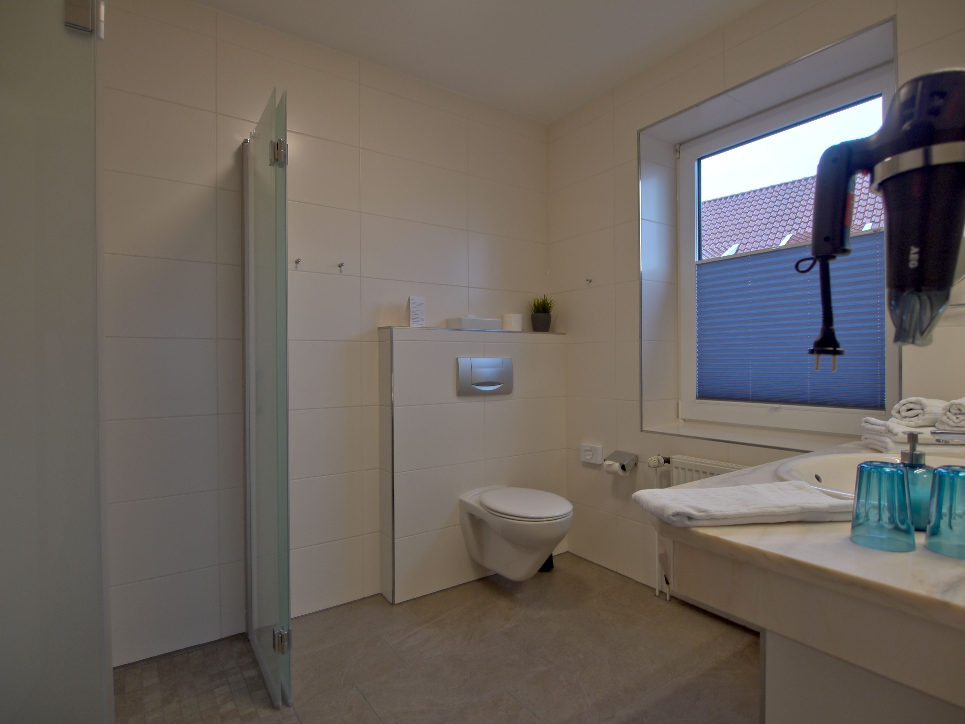 Un baño con inodoro, cabina de ducha de vidrio, lavamanos con toalla y ventana con persianas.