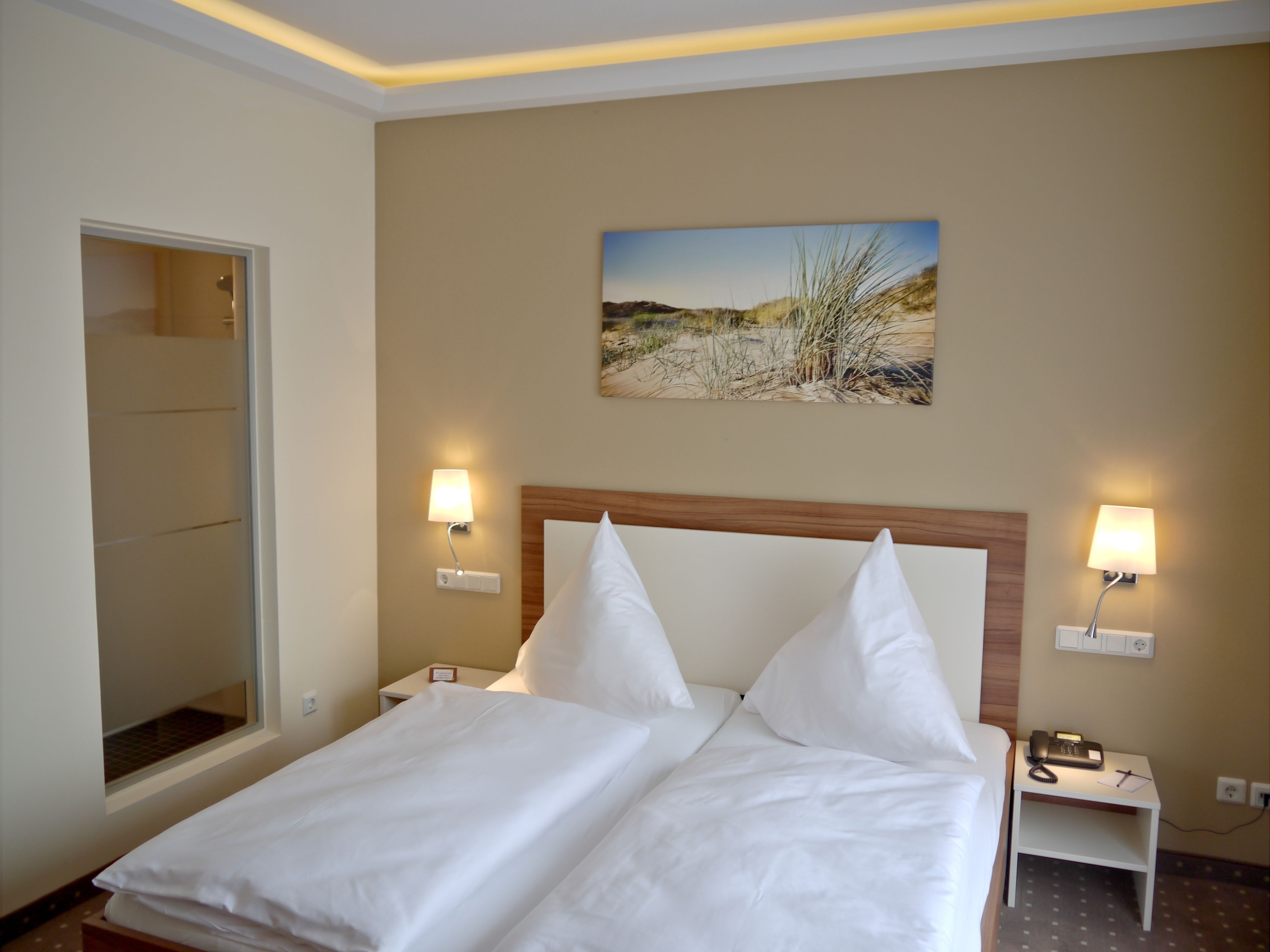 Ein Hotelzimmer mit einem Bett, zwei Nachttischen, einem Schreibtisch und einem Bild an der Wand sowie einem Fenster.