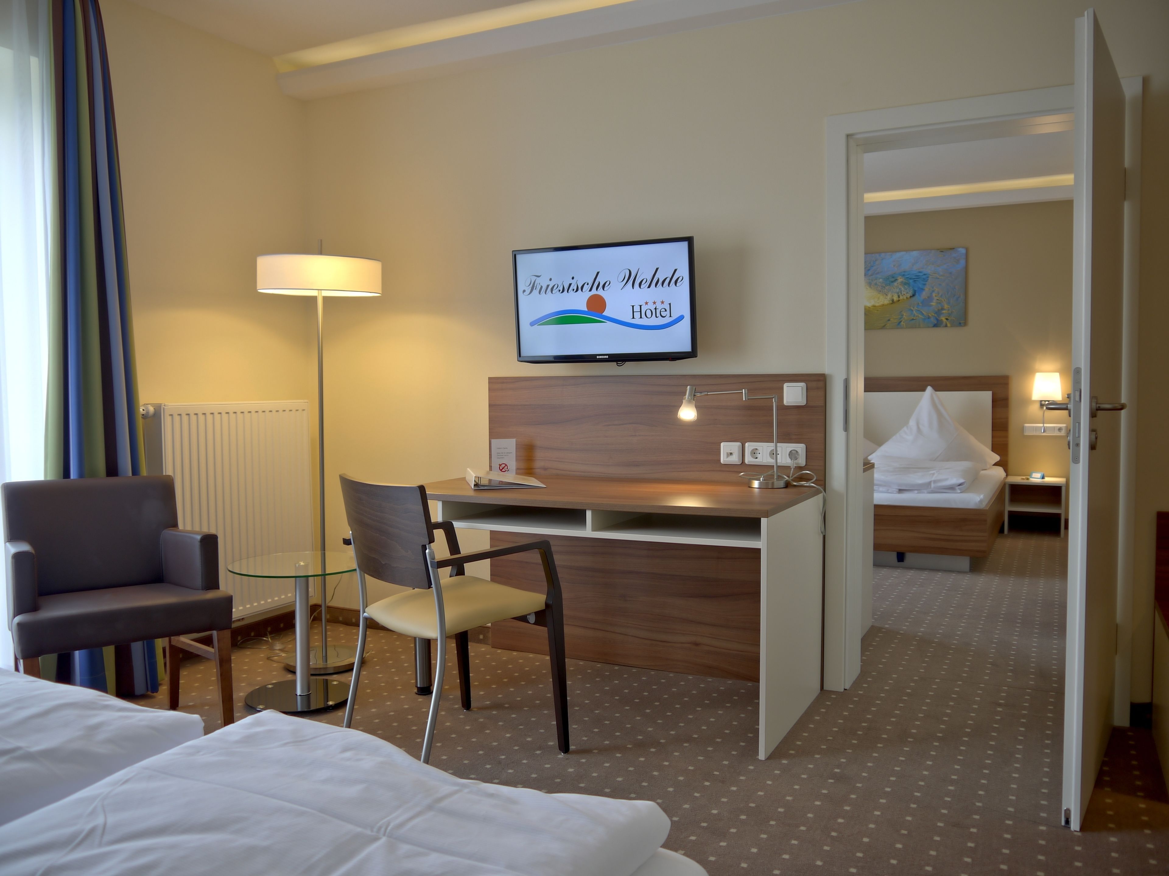 Une chambre d’hôtel avec un lit, un bureau, une chaise, une télévision et un oreiller blanc sur le lit.