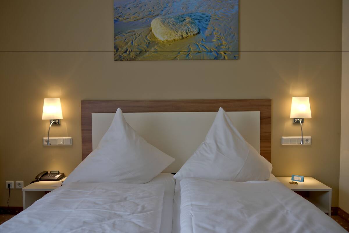 A hotel room with two beds, a wooden headboard, bedside lamps, a phone on the nightstand, and a painting on the wall.