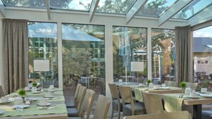 A restaurant with multiple tables and chairs, large windows, and a glass ceiling. - Hotel Friesische Wehde (Bockhorn)