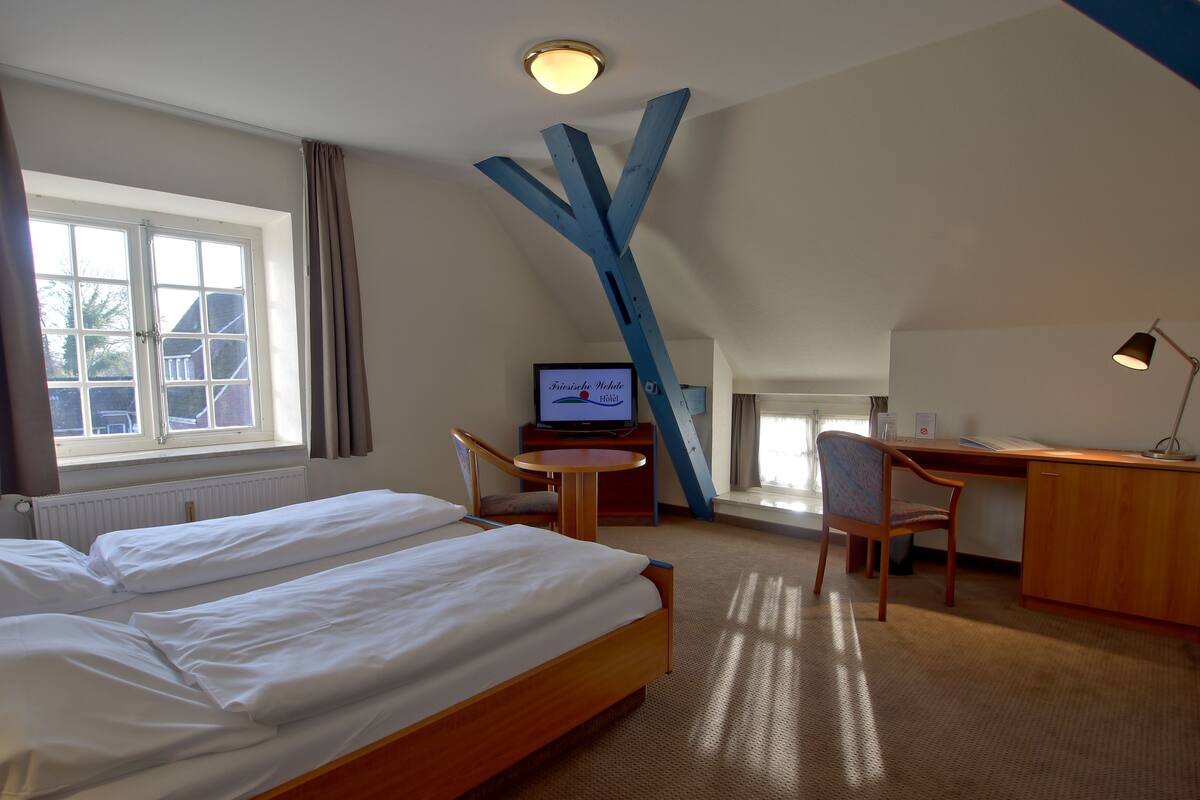 A hotel room with two beds, a desk, a chair, a television, and a view of the outside.