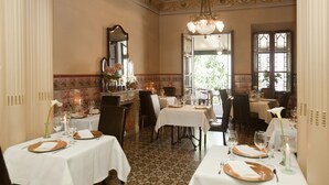 A dining area with multiple tables set for a meal, a chandelier, and a large mirror on the wall. - Hotel La Vila (Sóller)