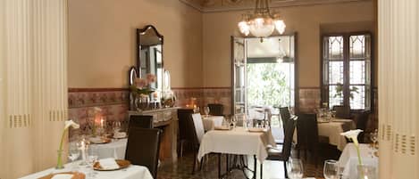 Une salle à manger avec plusieurs tables dressées pour le repas, un lustre et un grand miroir au mur.