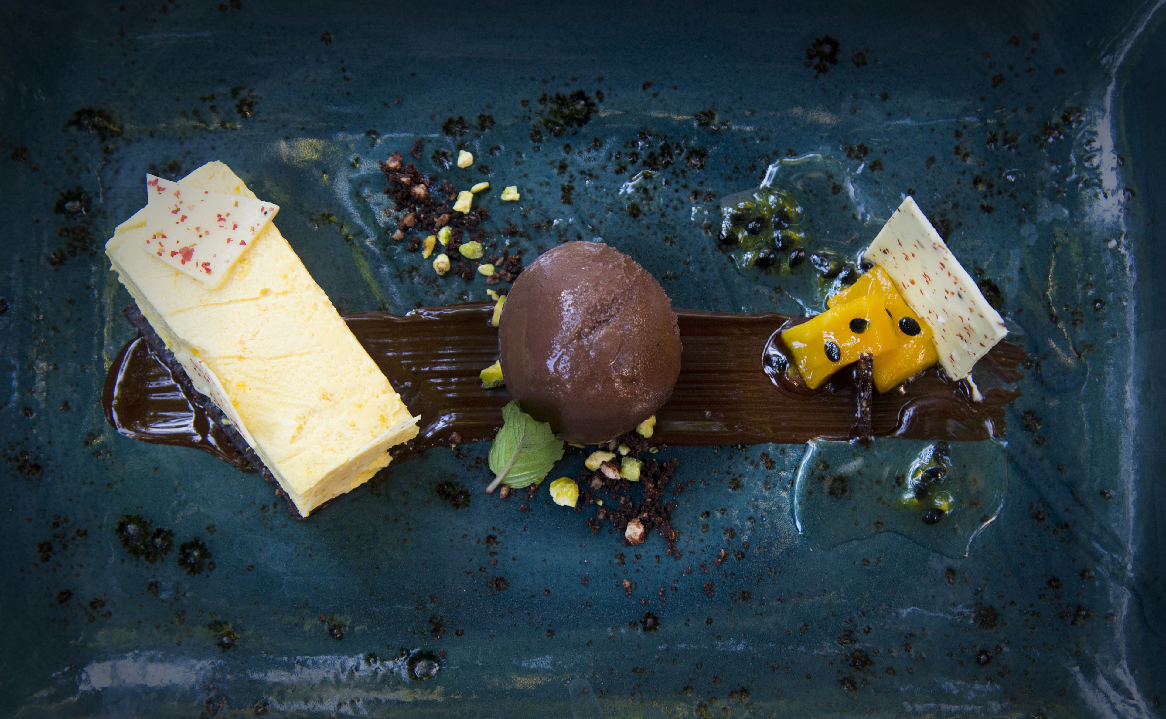A dessert with chocolate and yellow elements on a dark plate.