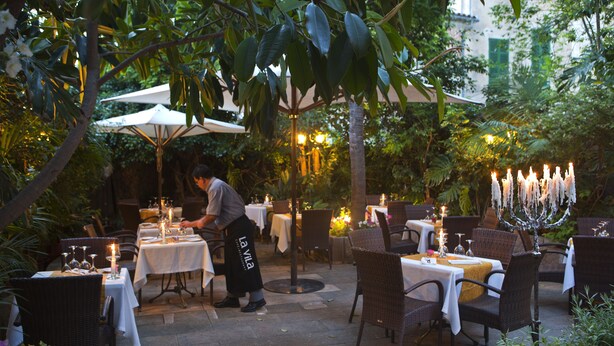 An outdoor dining area with tables and chairs, a waiter, and a decorative candle arrangement. - Hotel La Vila (Sóller)
