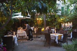 An outdoor dining area with tables and chairs, a waiter, and a decorative candle arrangement. - Hotel La Vila (Sóller)