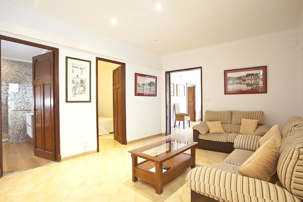 A spacious living room with a large sofa, a glass coffee table, and framed pictures on the walls. - Hotel La Vila (Sóller)
