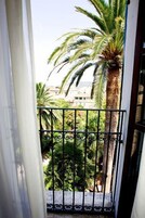 A balcony with a wrought iron railing, a palm tree, and a view of buildings in the background.