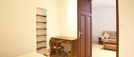 Une chambre à coucher comprenant un lit, un bureau en bois, une chaise, une armoire et un petit canapé dans la pièce adjacente.