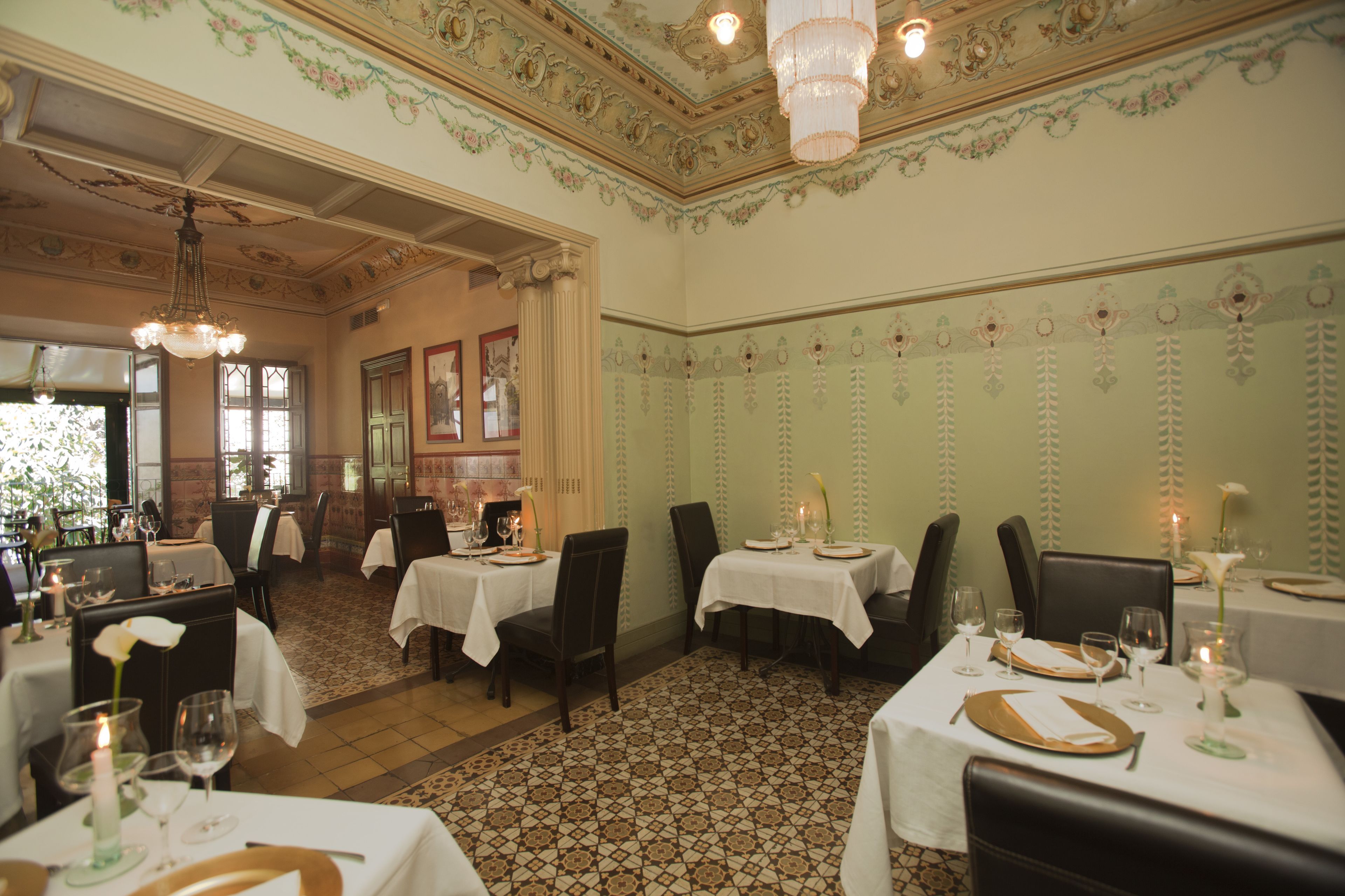 A dining area with tables set for service, chairs, and a chandelier.