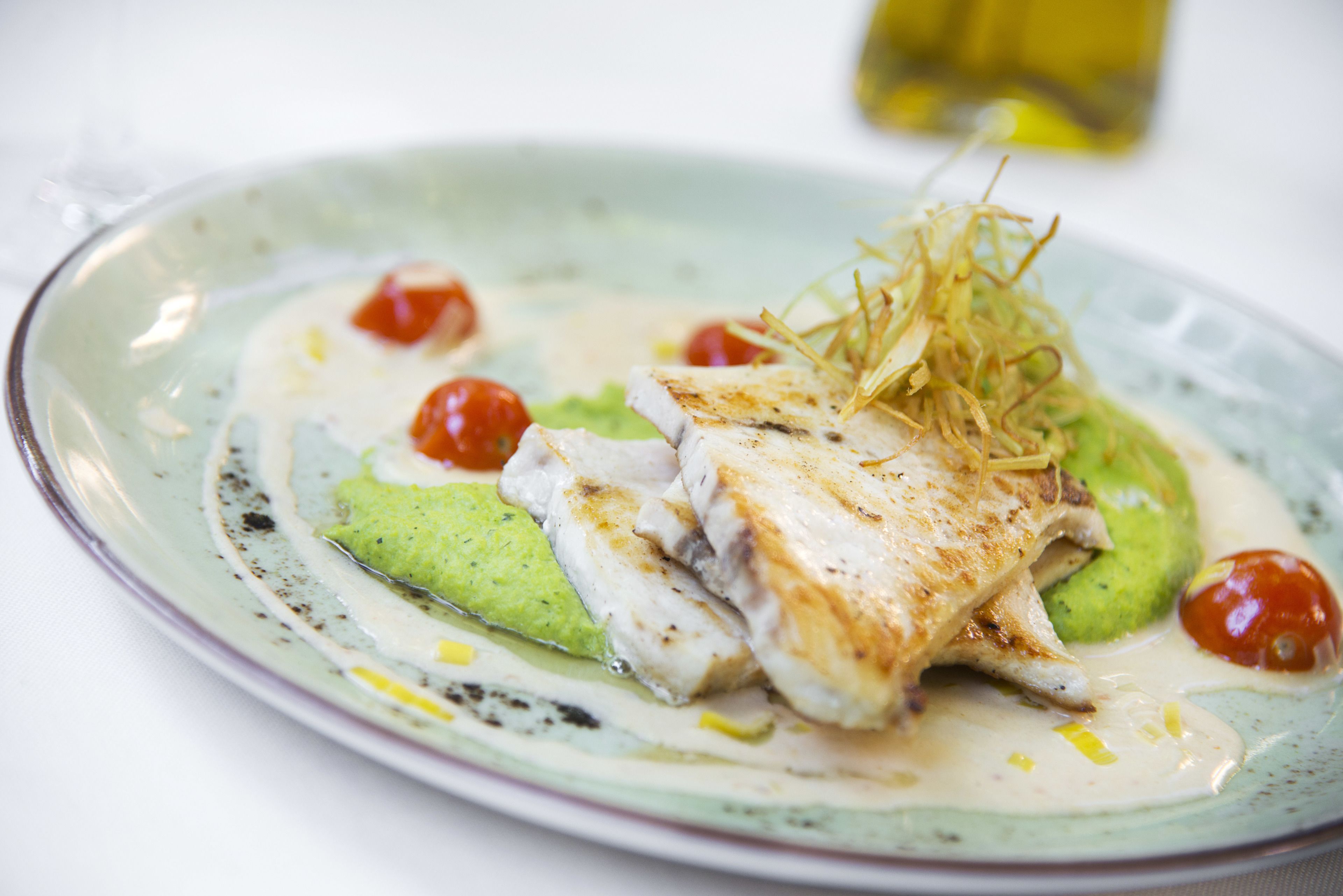 Un plato de comida con un trozo de pescado, verduras verdes y tomates cherry.