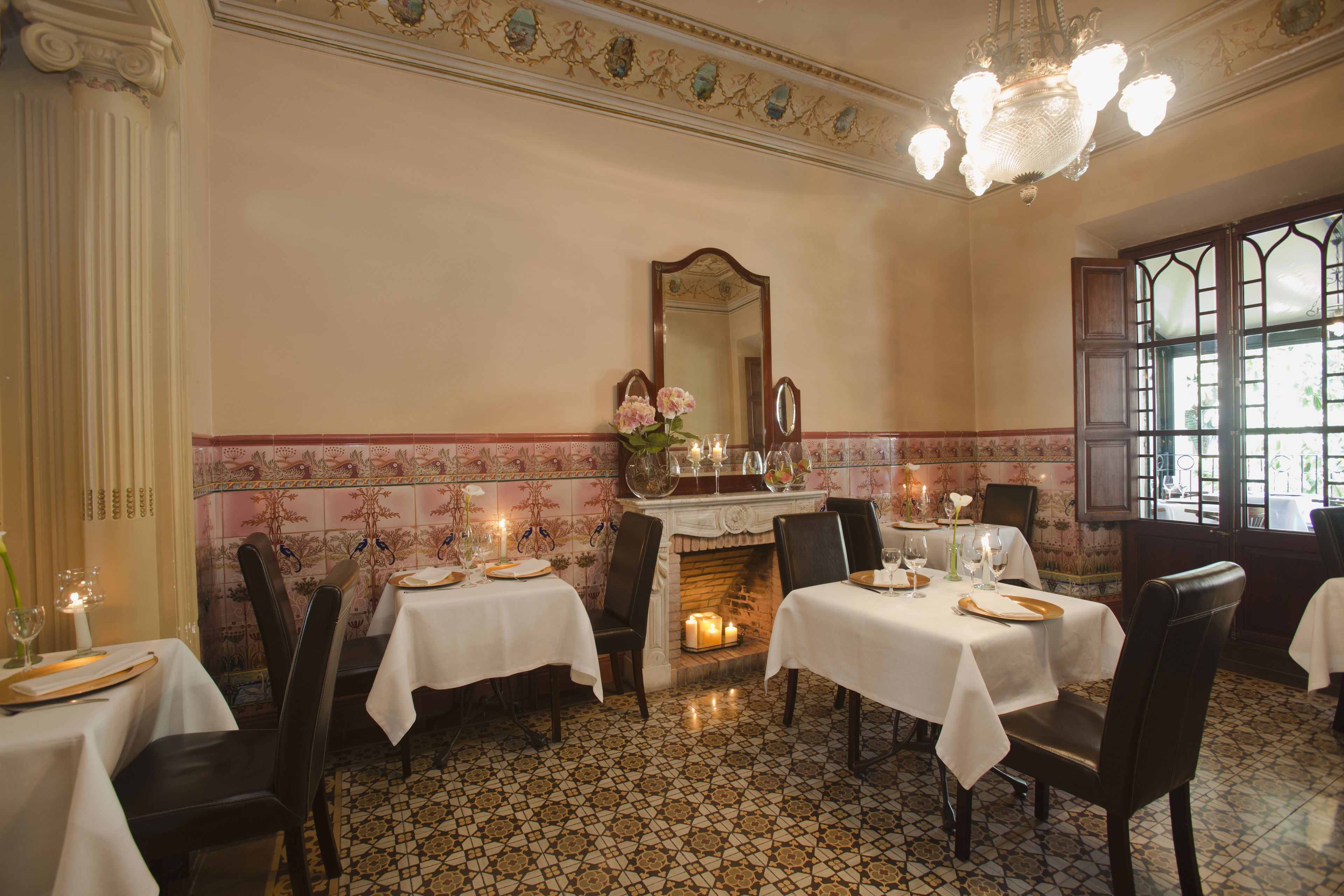 Un comedor con mesas preparadas para dos, una chimenea y un espejo grande en la pared.
