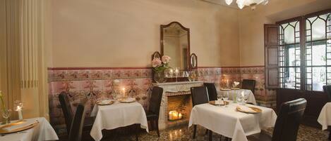 A dining area with tables set for two, a fireplace, and a large mirror on the wall.
