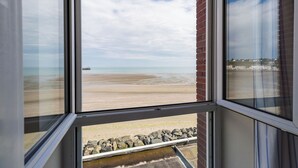 A view from a window overlooking a beach with a rocky barrier and a distant ship. - Hôtel Miléade de la Plage - Binic (Binic-Etables-sur-Mer)
