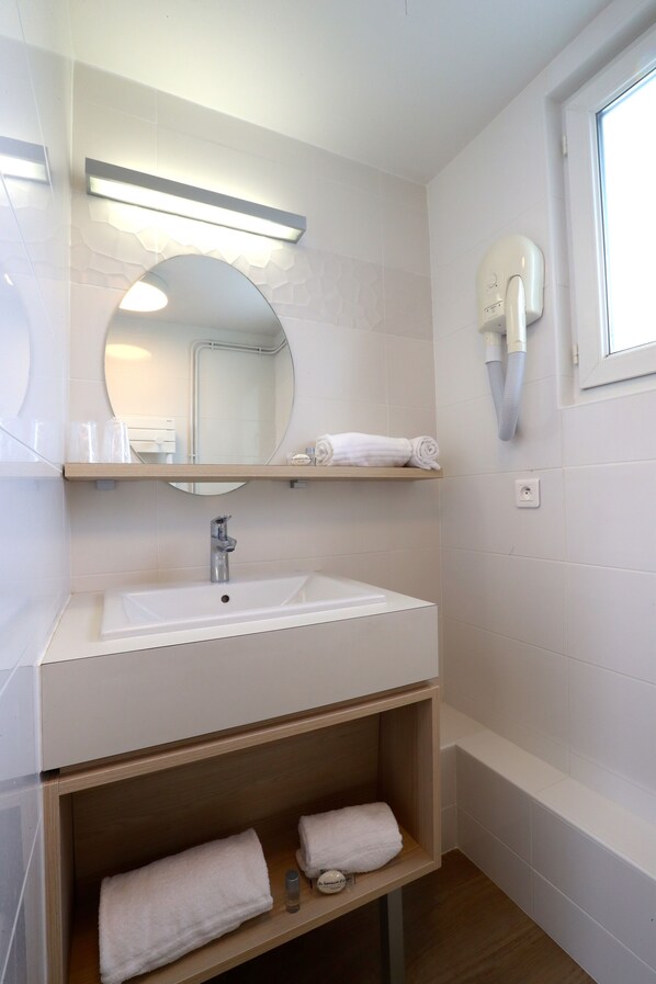 Un baño moderno con un lavabo blanco, espejo y barras para toallas.