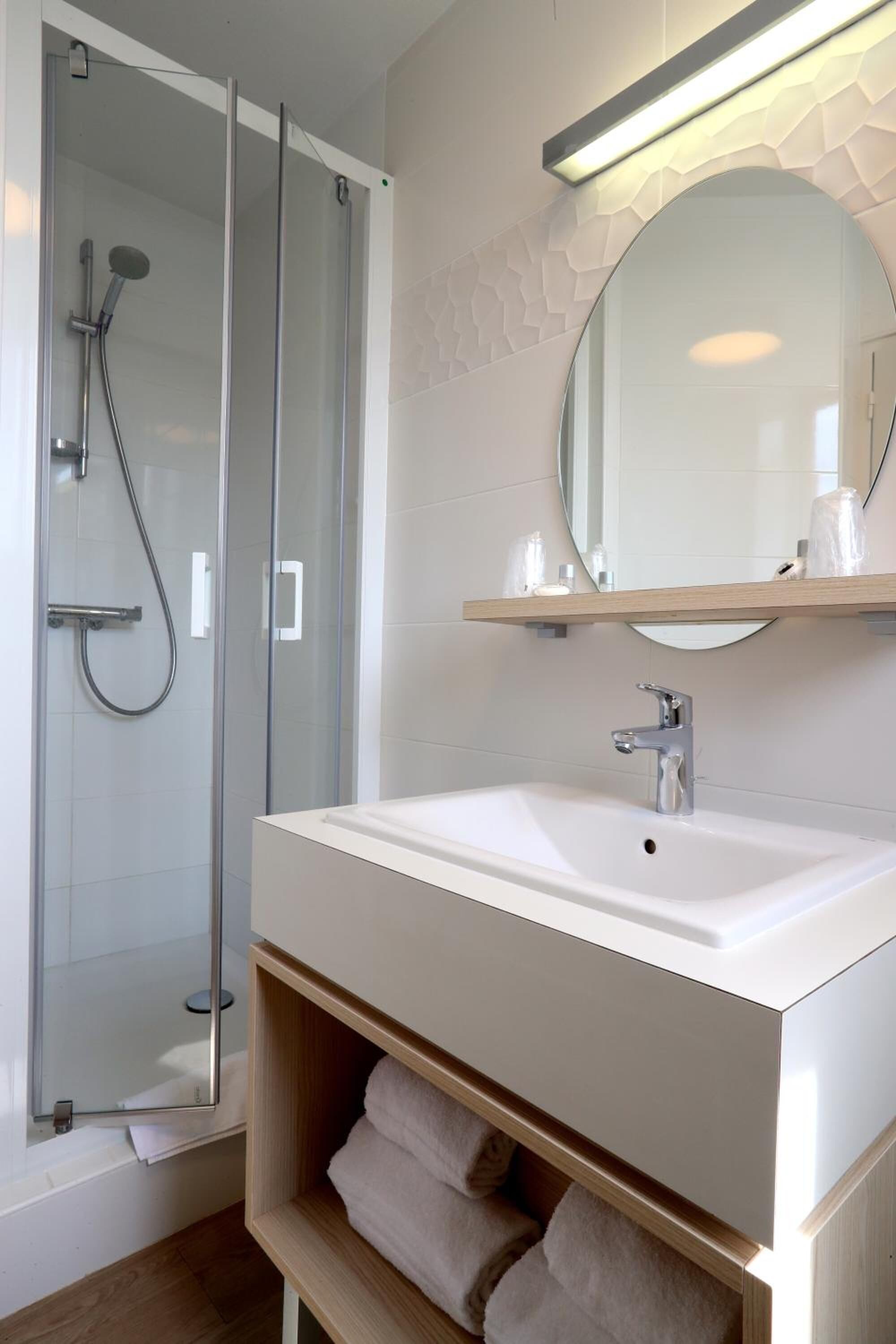 Een moderne badkamer met een douchecabine van glas, een witte wastafel en een spiegel erboven.