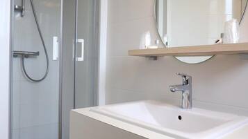 Een moderne badkamer met een douchecabine van glas, een witte wastafel en een spiegel erboven.