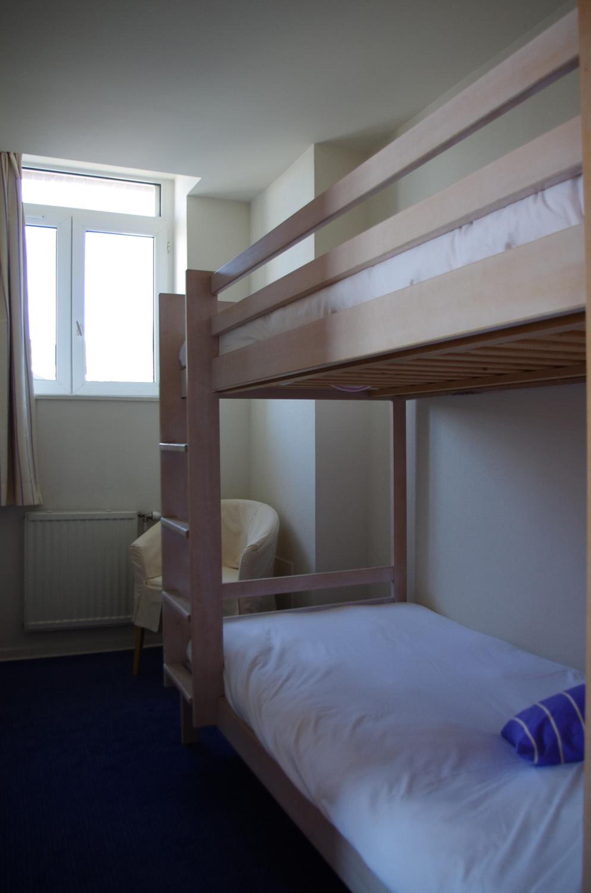 Une chambre avec un lit superposé, une fenêtre, une chaise et un radiateur.