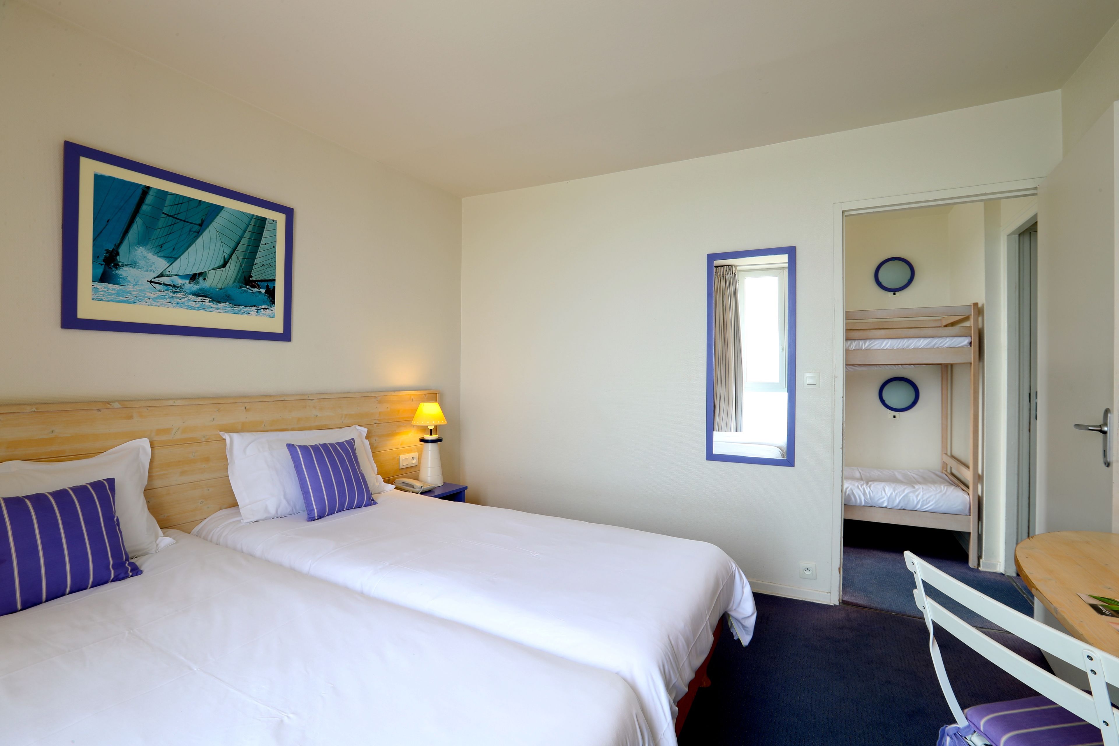 Ein Hotelzimmer mit zwei Betten, einem Holzkopfende, einem Nachttisch mit Lampe, einem gerahmten Bild an der Wand und einem Schlafsofa in der Ecke.