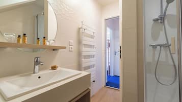 Een moderne badkamer met een wit wastafelmeubel, spiegel en douche. Handdoekrek aanwezig en een plank met toiletartikelen.
