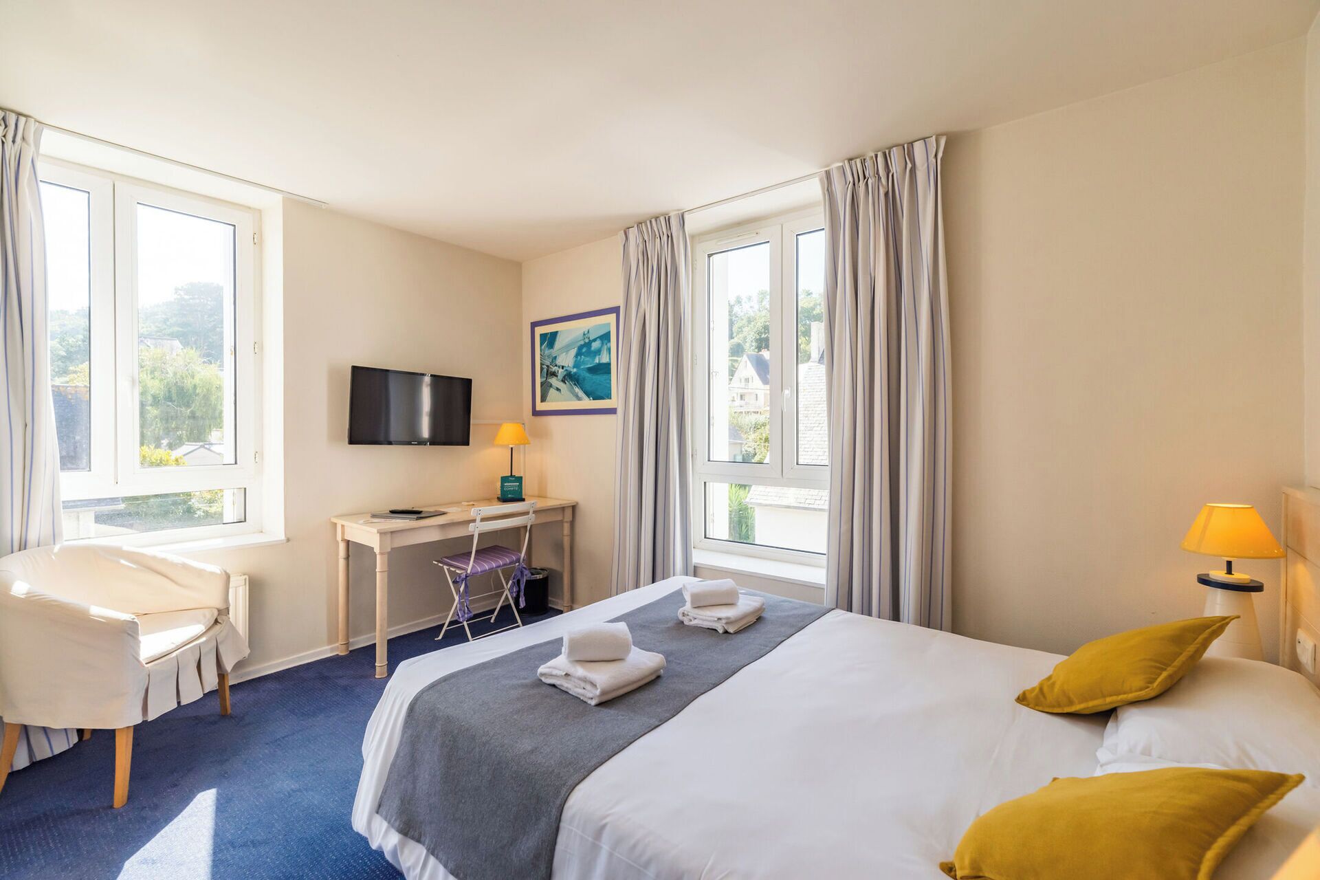 A hotel room with a bed, a desk, a chair, a TV, and a window with curtains.