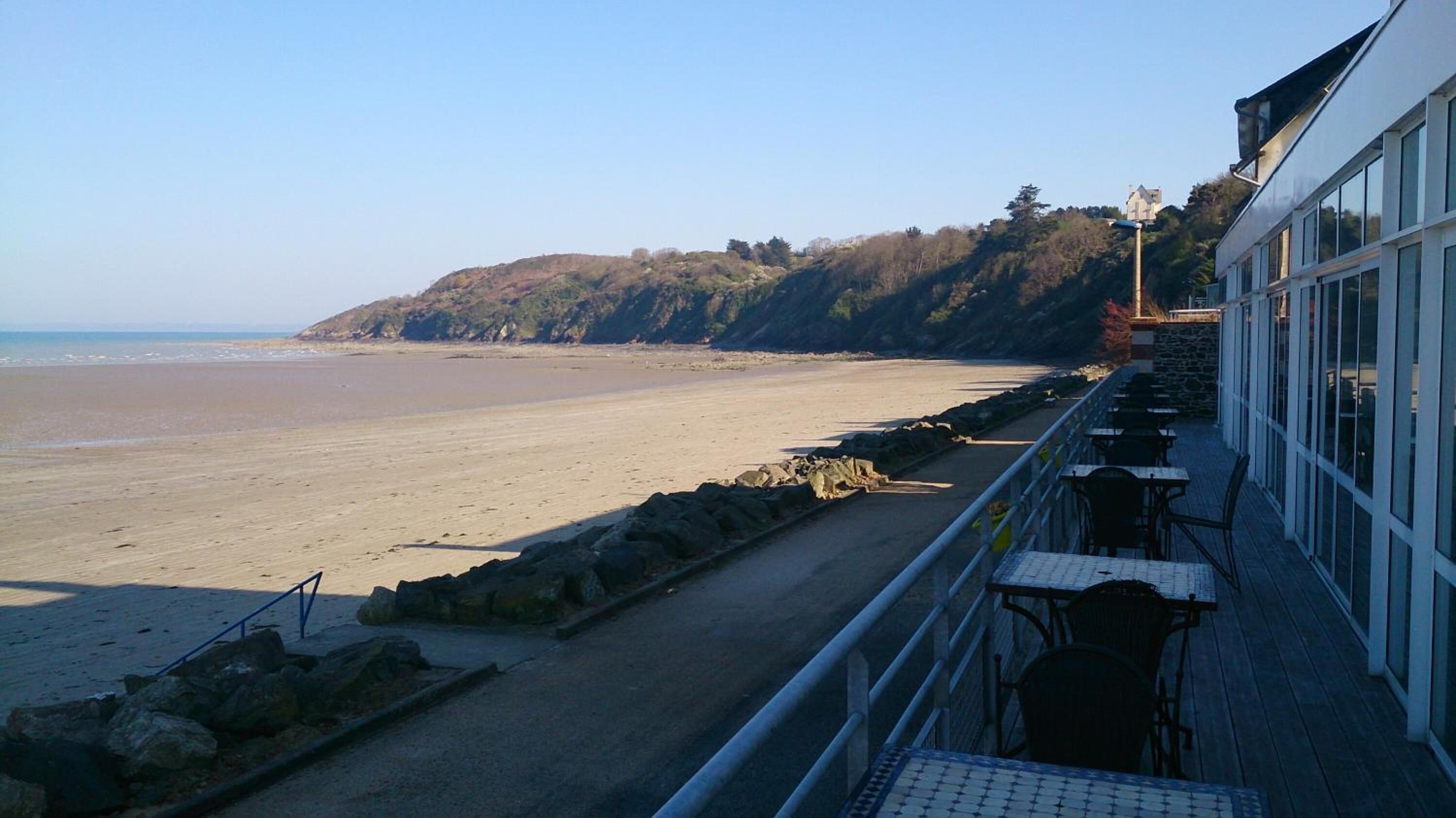 Une vue sur la plage, avec un rivage rocheux, un ciel dégagé et un bâtiment doté d’une terrasse.
