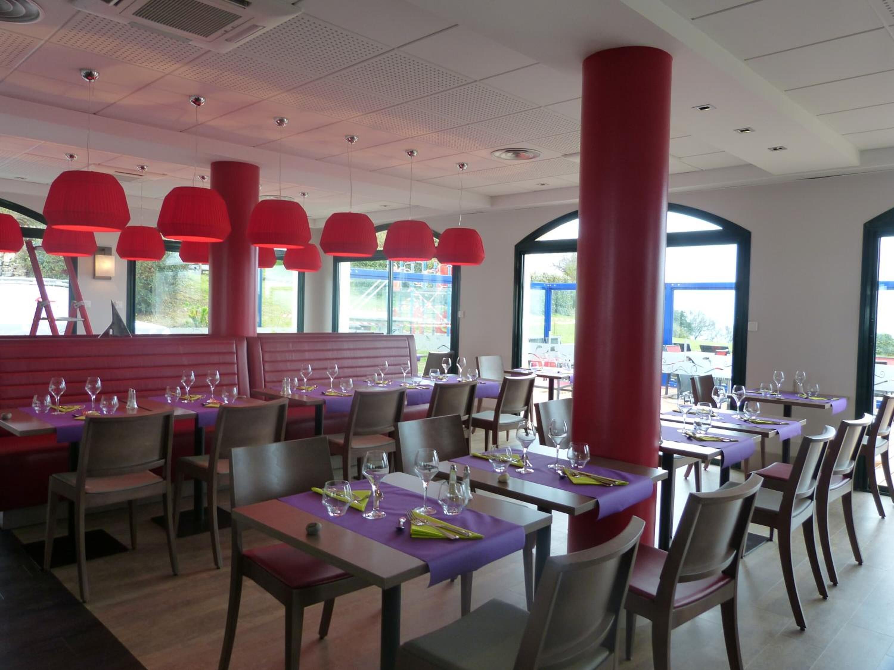 Een restaurant met gedekte tafels, rode zuilen en hanglampen.