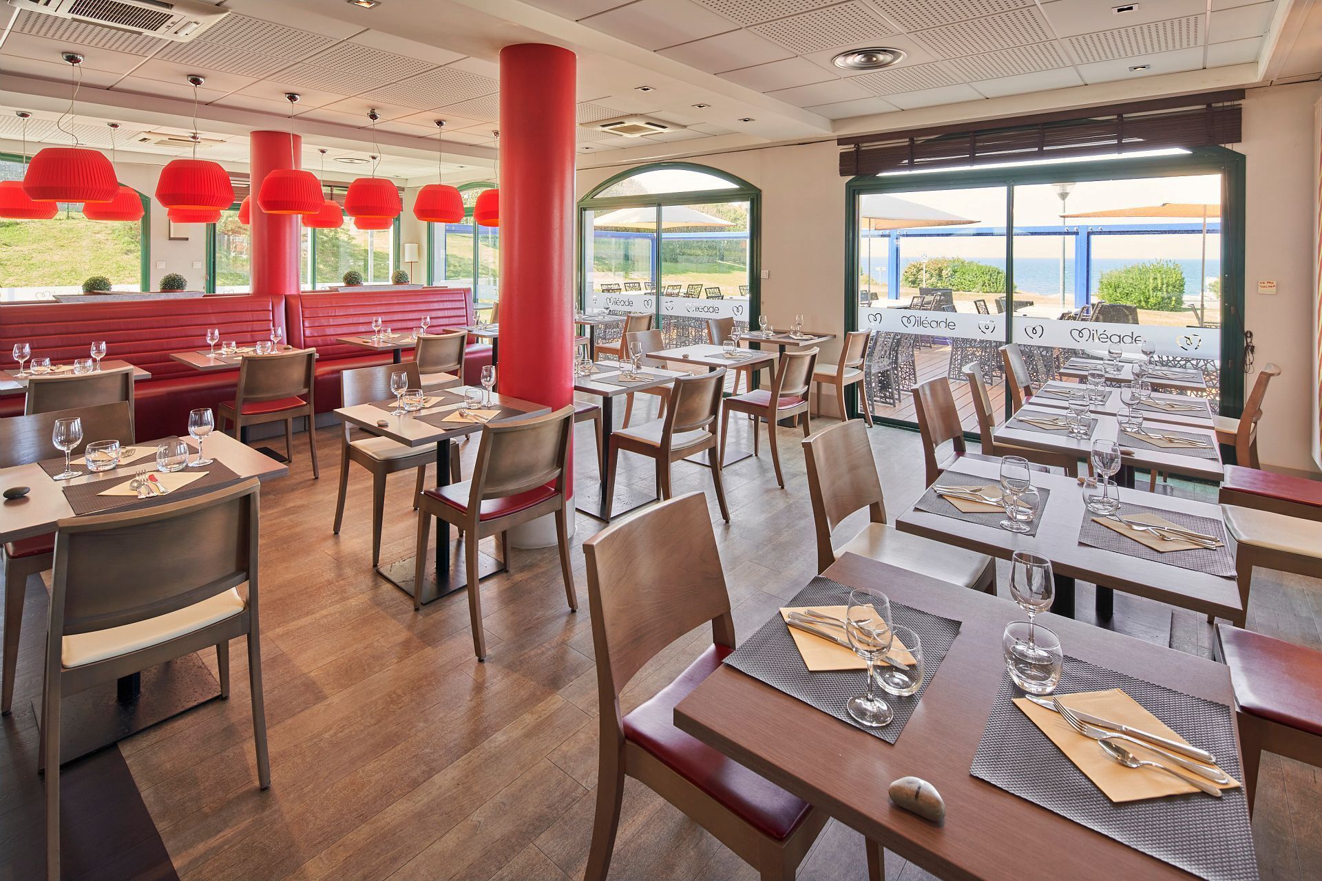 A restaurant with red booths and tables, large windows, and red pendant lights.