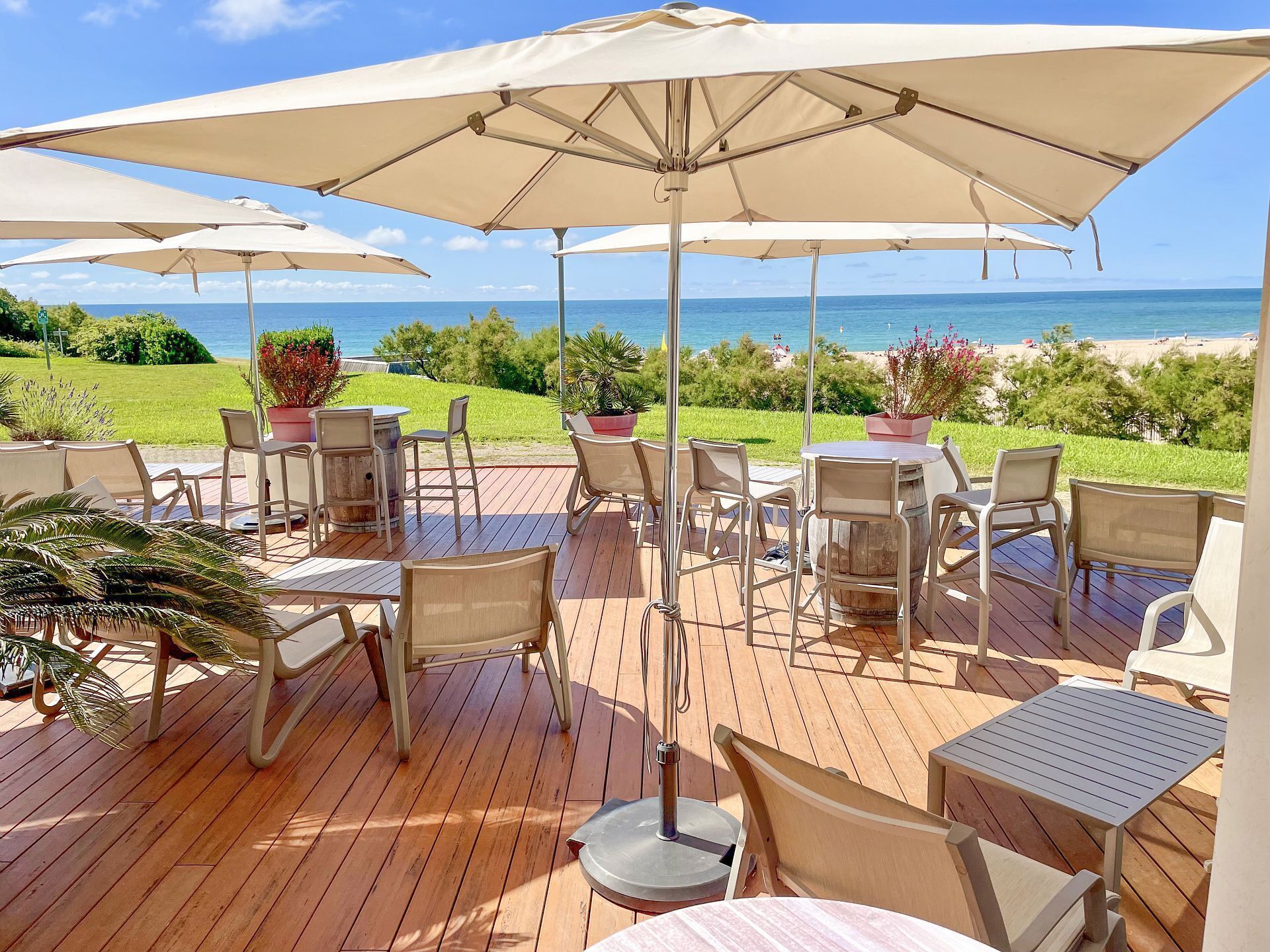 An outdoor patio with wooden flooring, beige chairs, and umbrellas providing shade.