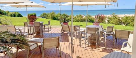 An outdoor patio with wooden flooring, beige chairs, and umbrellas providing shade.