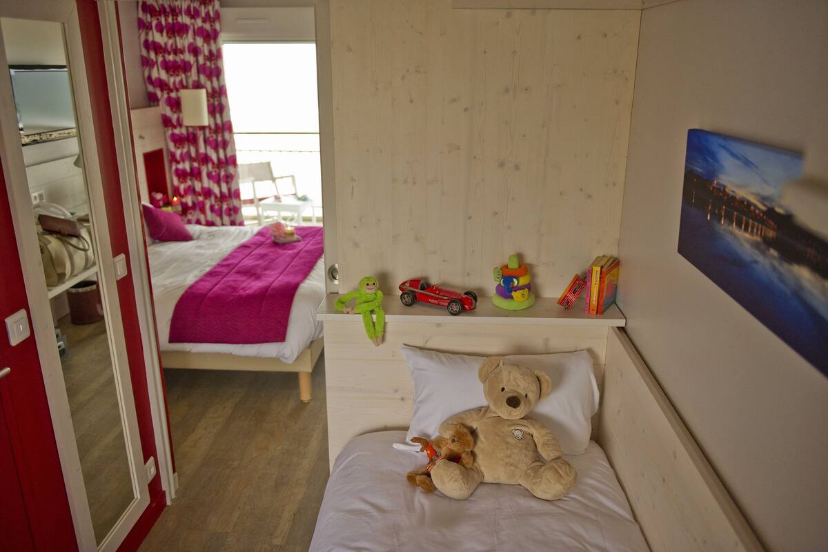 A bedroom with a bed, a teddy bear, and children's toys on a nightstand.