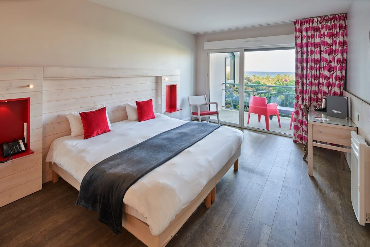A hotel room with a large bed, a desk, a chair, and a balcony with a view.