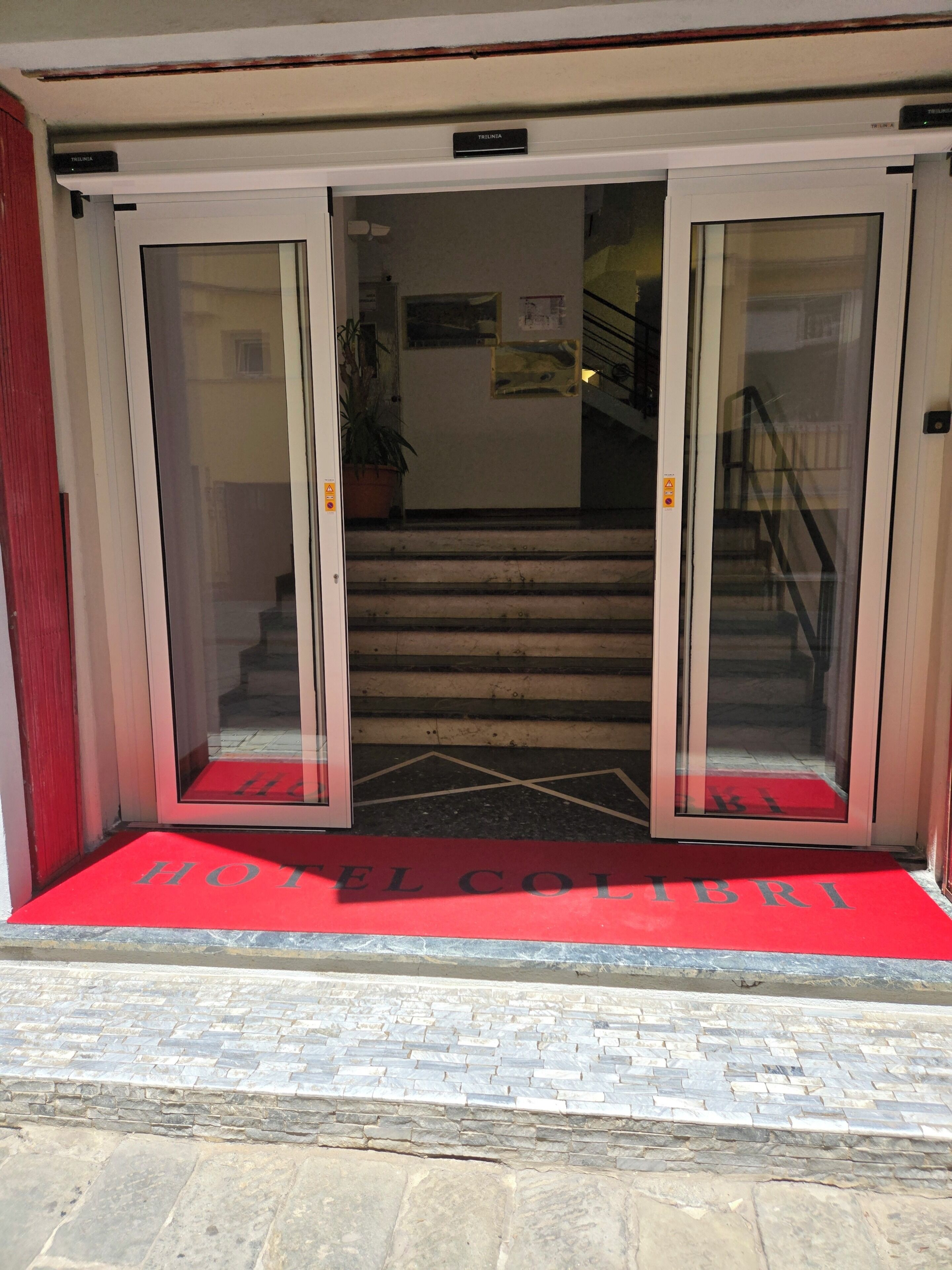 A hotel entrance with a red carpet, double glass doors, and a staircase leading inside.