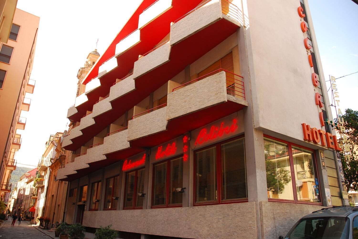 A hotel with a red and white facade, multiple balconies, and large windows.
