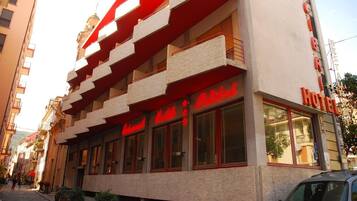 A hotel with a red and white facade, multiple balconies, and large windows.