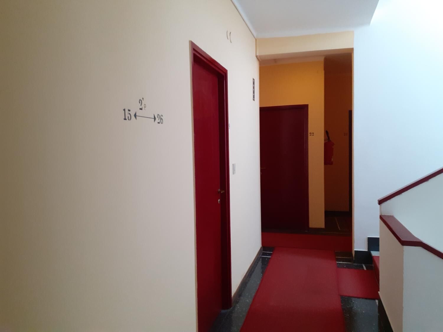 Un pasillo con puertas rojas, numeradas del 15 al 26, y una alfombra roja.