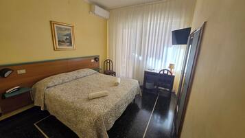 Una habitación de hotel con cama, escritorio, silla, televisor y un cuadro en la pared.