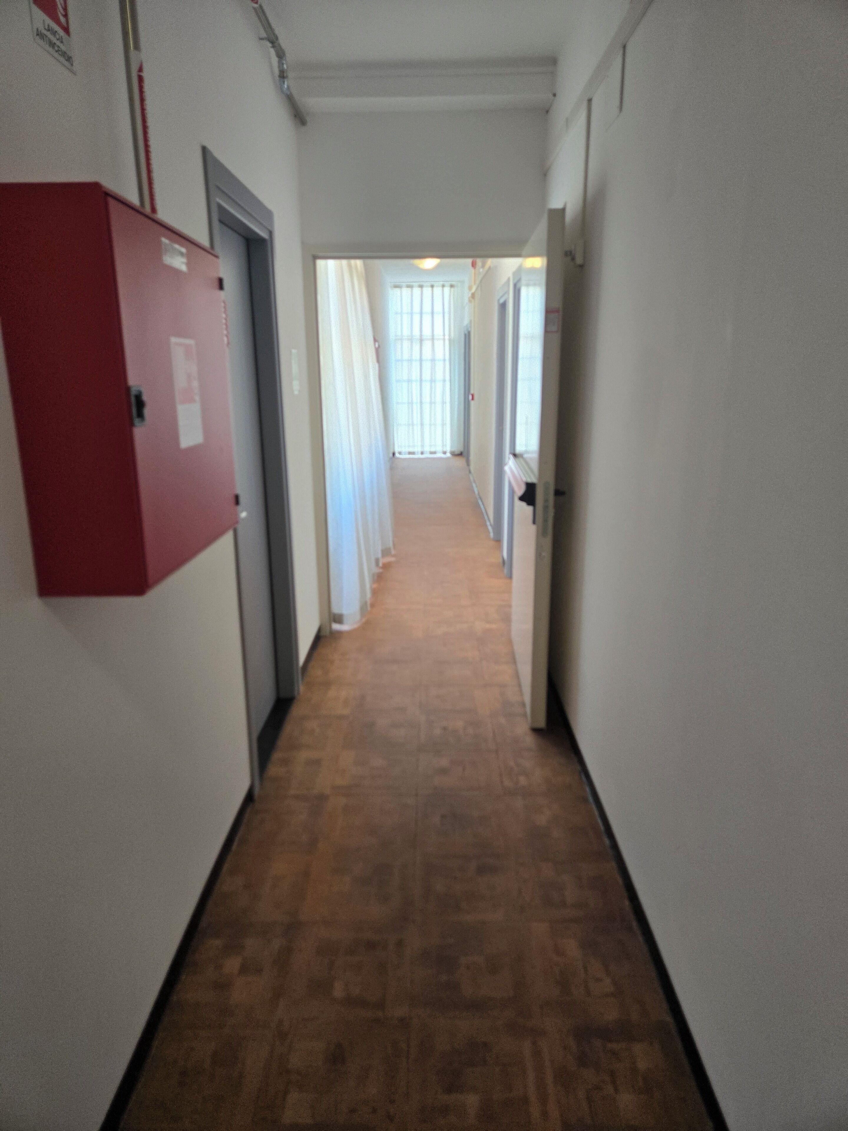 A hallway with a red utility box, a door, and a window with curtains.