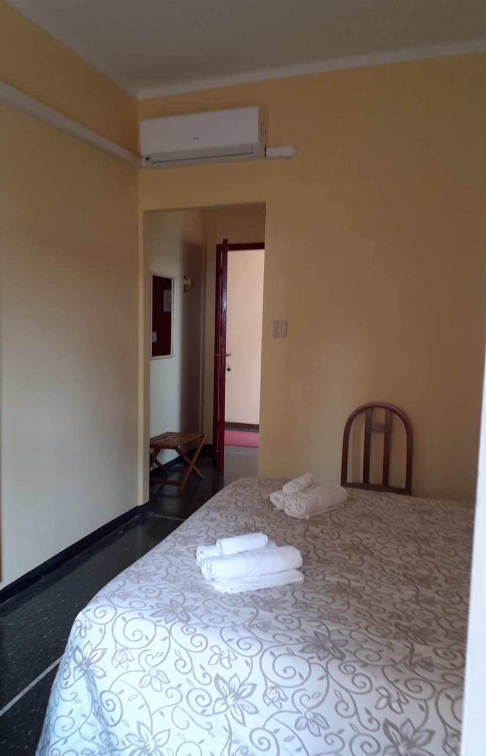 Una habitación de hotel con cama, una silla, escritorio y aire acondicionado.