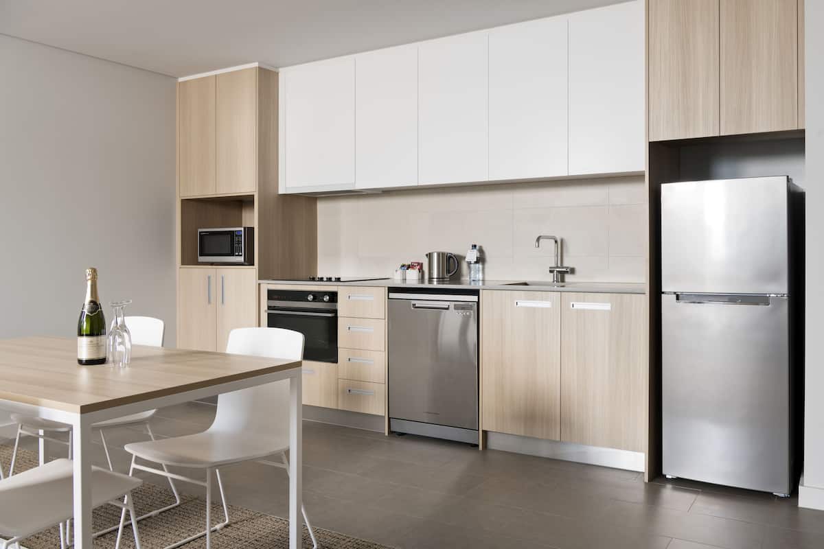 A modern kitchen with white cabinets, stainless steel appliances, and a wooden dining table with chairs.
