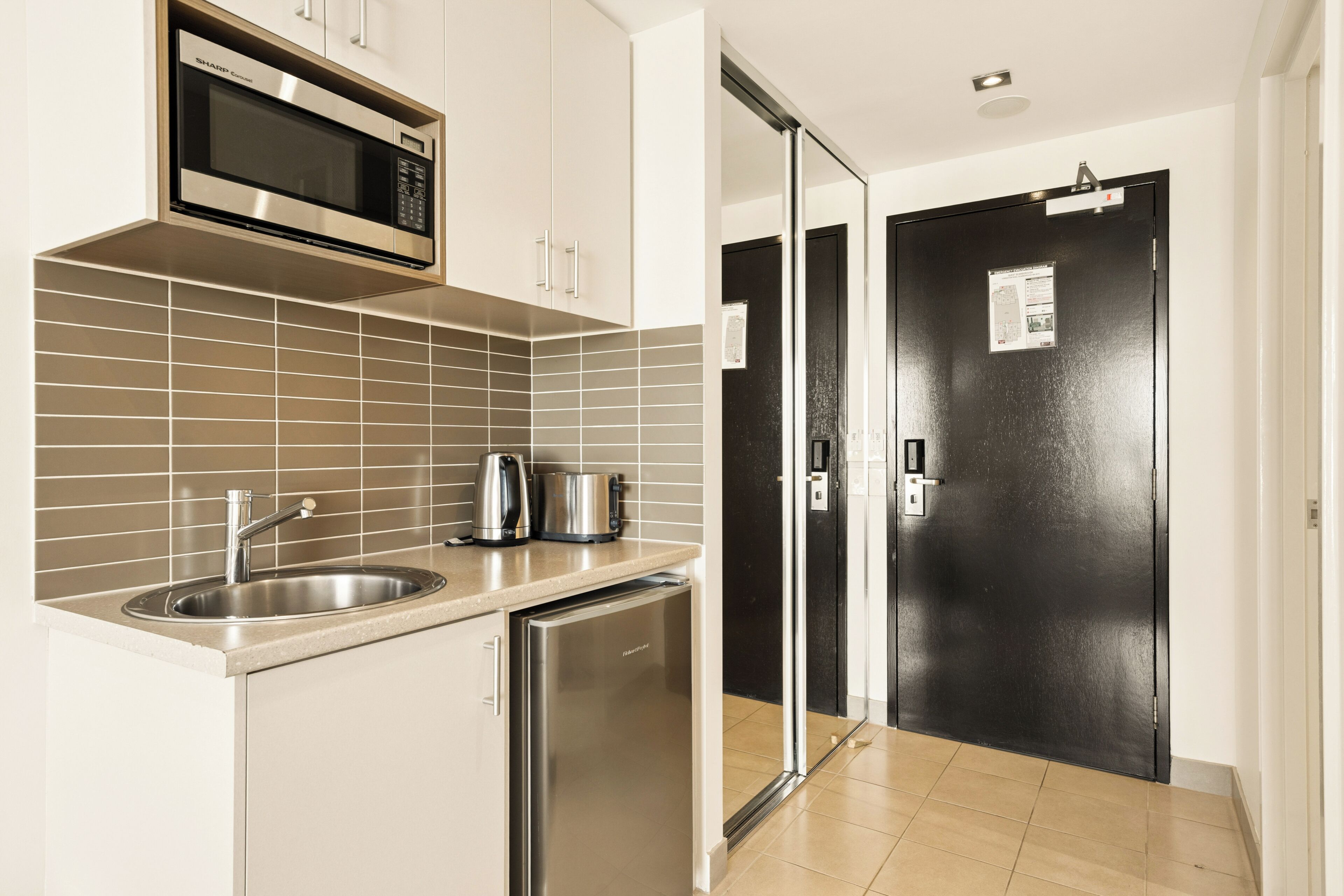 Een moderne keuken met een magnetron, spoelbak, waterkoker en koelkast.