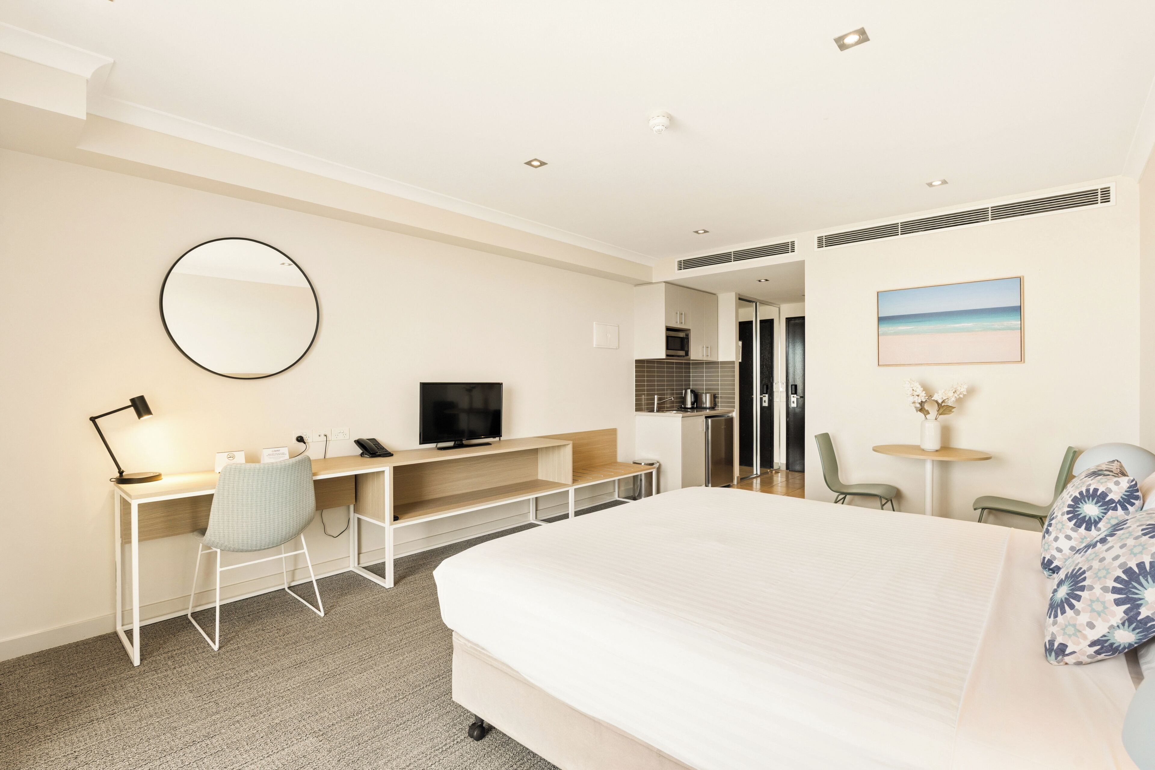 Een hotelkamer met een bed, bureau, stoel, televisie en een kleine kitchenette.