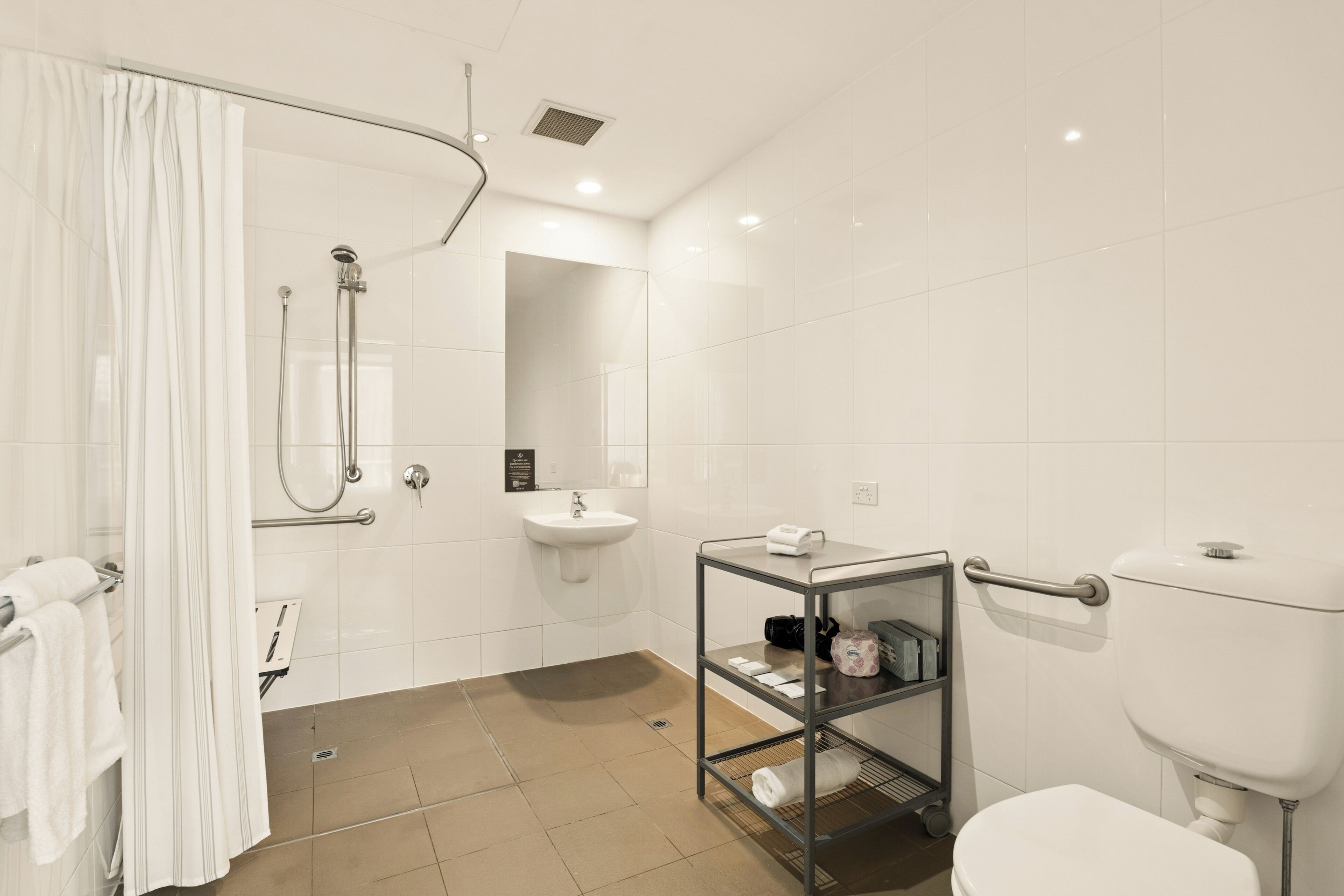 Un baño moderno con ducha, inodoro, lavamanos y un estante de vidrio con artículos de aseo.