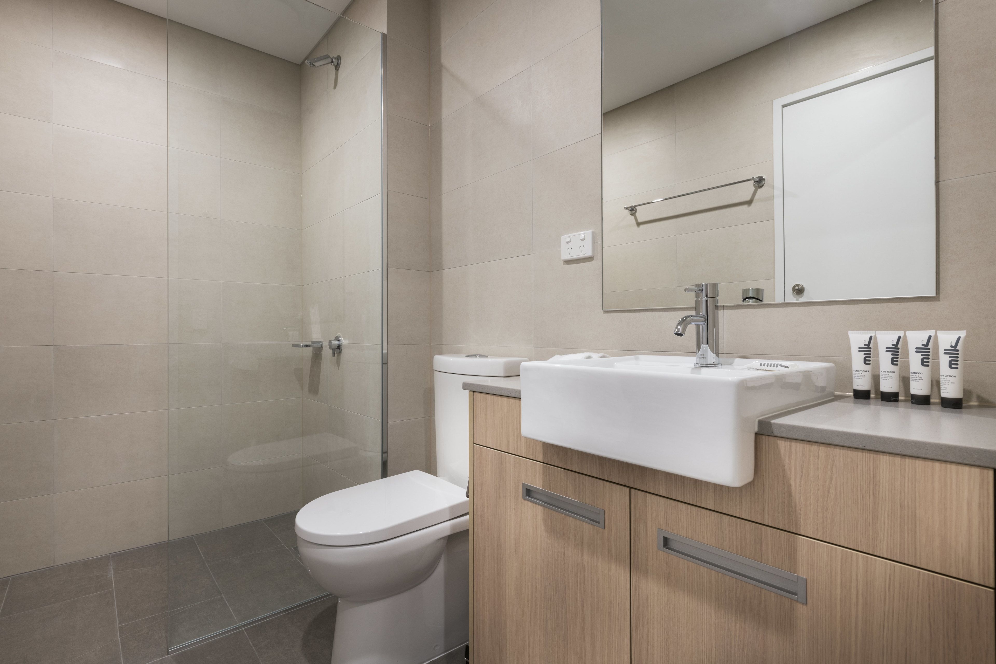 Une salle de bain moderne avec une douche à parois de verre, des toilettes blanches, un lavabo avec un miroir au-dessus et des articles de toilette posés sur le comptoir.