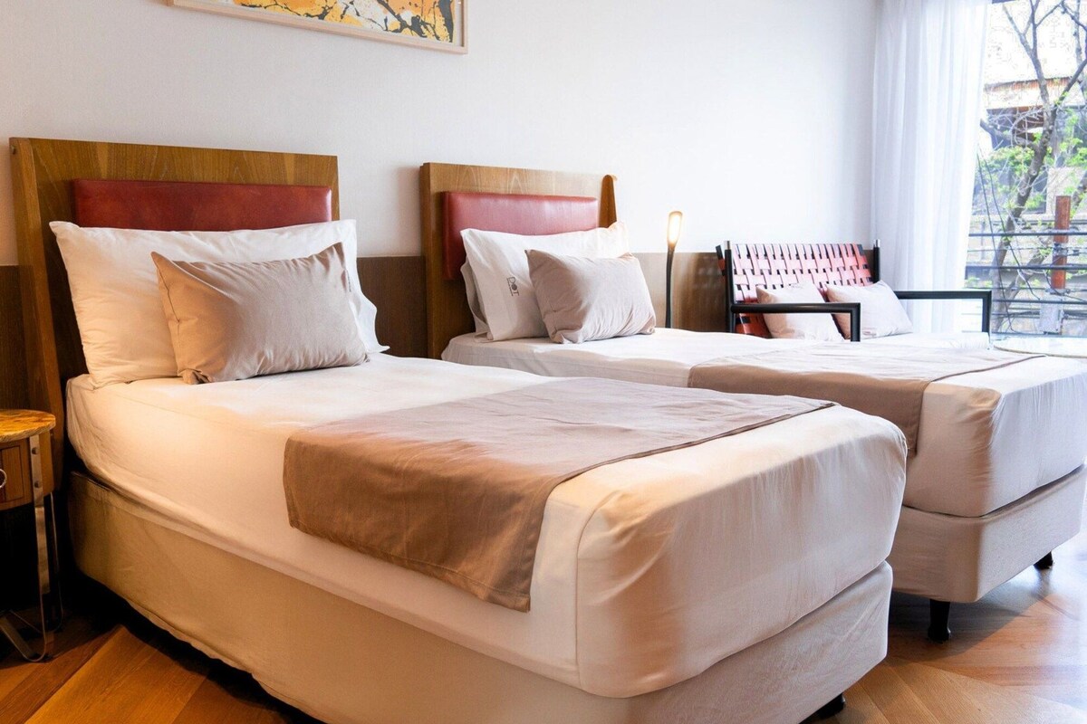 Habitación de hotel con dos camas, cabecera de madera y ventana con vistas.